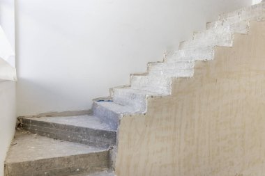 Tamamlanmamış beton merdiveni olan boş bir daire, arta kalan malzemeler ve beyaz duvarlar, ev inşaatı veya tadilatı. Tamamlanmamış konut binasının içi. Mimari ilerleme