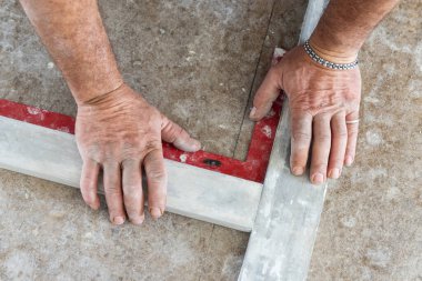 Marangoz fayanstan önce evin zeminindeki açıları ölçüyor. Eller yakın. Ev iç dekorasyonu. Yeni bir binanın inşaatı 