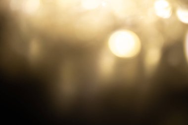 Altın kahverengisi Noel arkaplanı. Bulanık beyaz çelenk ışıkları arka planda parıltılar ve sunum için yumuşak yansımalar, tebrik kartları ve kartpostallar. Bulanık klasik altın soyutlaması.