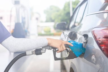 Close up hand of refueling worker are filling fuel to car in Petrol station. Focus on fuel nozzle and blur day light background