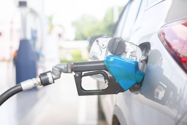 Close up hand of refueling worker are filling fuel to car in Petrol station. Focus on fuel nozzle and blur day light background