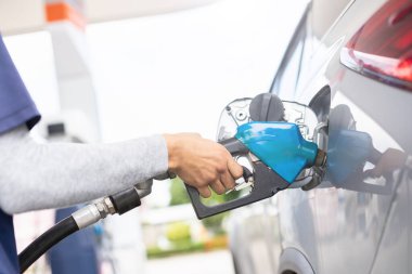 Close up hand of refueling worker are filling fuel to car in Petrol station. Focus on fuel nozzle and blur day light background