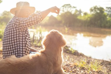 Asian man sitting at the river with smart brown Golden Retriever at morning time