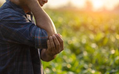 Injuries or Illnesses, that can happen to farmers while working. Man is using his hand to cover over elbow because of hurt,  pain or feeling ill. Health of agriculturist concept.