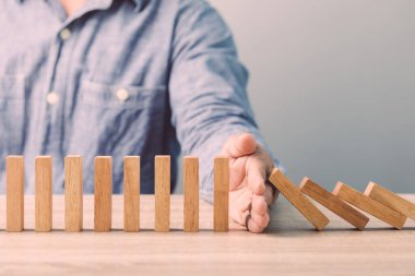 Businessman's hand stopping wooden block as domino on the desk. Ideas of business crisis effect or risk situation protection concect.