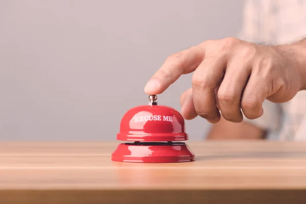 Close up hand ringing the red call bell or service bell ring on the brown wooden desk with grey wall background. For hotel or restaurant advertising concept