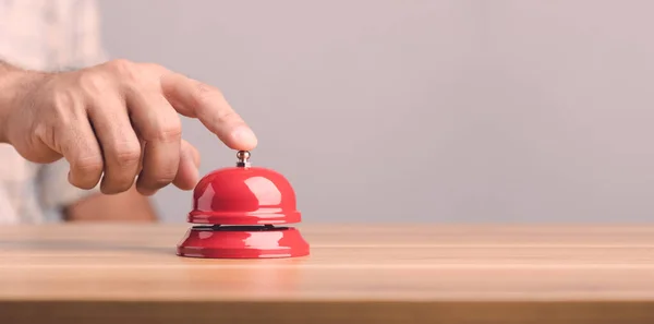 Close up hand ringing the red call bell or service bell ring on the brown wooden desk with grey wall background. For hotel or restaurant advertising concept