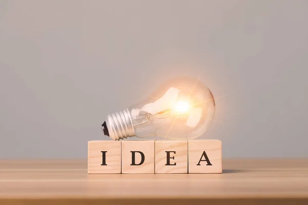 Close up clear light bulb with wooden blocks write IDEA. Put on wooden desk with grey space wall background. Start for new idea concept.