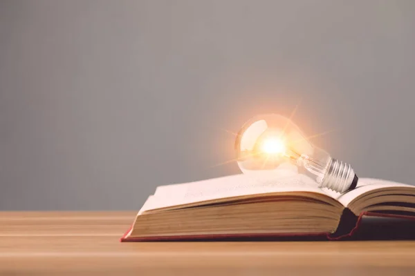 关闭明亮的灯泡 对旧书有灯光效果 并放置在灰色空间墙壁背景的木制书桌上 学习观念 教育观念 — 图库照片