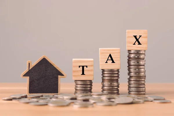 对房屋和房地产支付的税收概念 Tax写在木块上 放在写字台顶部的硬币堆栈上 有灰色的墙壁背景 金融想法 — 图库照片