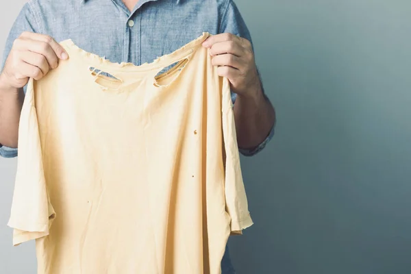 使用了错误类型的洗衣粉概念 男人拿着黄色撕破的旧T恤 工作室拍摄灰墙背景 — 图库照片