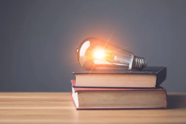 New inspiration for knowledge idea. Clear vintage light bulb with light effect on old book and put on wooden desk with gray space wall background. Idea of learning, Education concept. Studio shot.