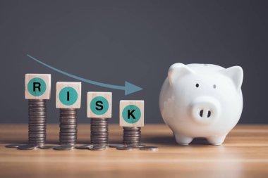 Finansal sorun, iflas ya da iş konseptinde başarısızlık. Yeni domuz kumbarasının beyazı, bozuk para yığını ve kelime RİSK tahta bloğun küpüne yazılmıştı. Ahşap masa üzerine kurulmuştu..