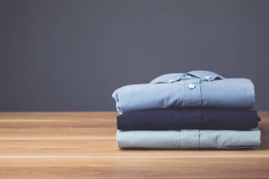 Ahşap masa üzerinde koyu gri arkaplanı olan yeni renkli erkek gömleği yığını kapat. Erkek giyim konsepti.