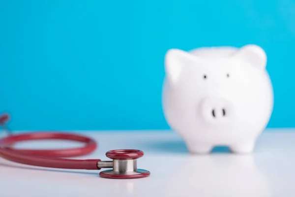 Financial health check, The idea of taking care of saving money, Man using stethoscope to check white piggy bank on desk with grey copy space background. Health and finance concept