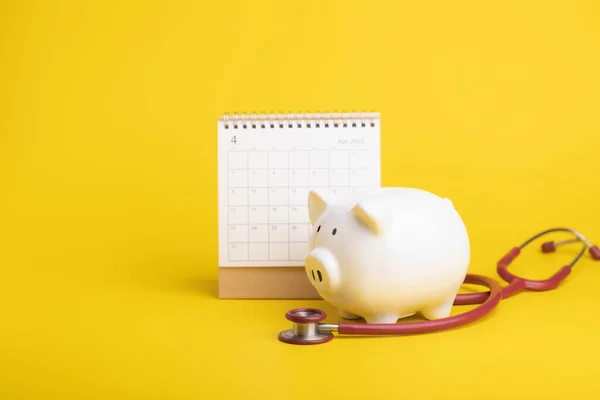 Financial for health concept, The idea of saving money for healthcare, Close up stethoscope, calendar and white piggy bank on yellow background. Time for health check up and finance concept.