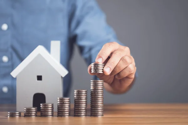 Money saving for house or Financial for real estate concept. Man stacking coin and small house model on the wooden table. Keeping fund for purchase the residence idea. Studio shot on grey background.