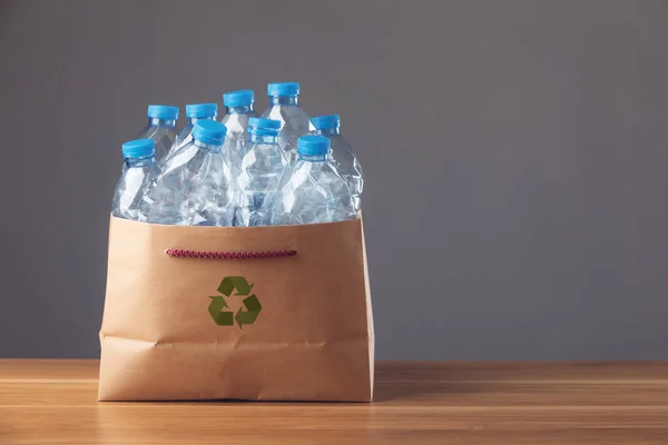 拯救世界和环境的概念 在木制书桌和深色背景的褐色纸袋中使用蓝色塑料瓶 可用于重复使用 循环利用和环境概念 工作室拍摄 免版税图库照片