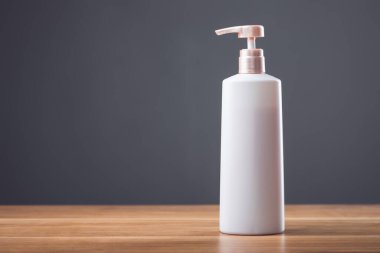 Koyu gri arkaplanı olan ahşap bir masada beyaz şampuan şişesi. Reklamcı güzellik ürünleri için mükemmel.