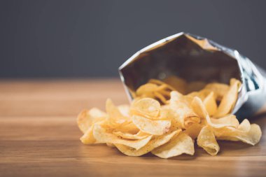 Koyu gri arka planda tahta bir masaya yerleştirilmiş patates cipslerinin yakın çekimi. Sağlıklı yeme kavramı.