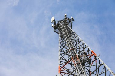 A cellphone tower stands tall against the sky, its structure silhouetted by the vast blue backdrop. The image captures the intersection of technology and the natural world. clipart