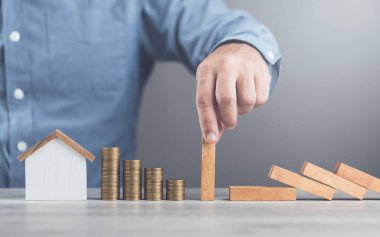 İşadamı, kaynakların etkin bir şekilde yönetilmesi, domino etkisi ve risk yönetimi alanlarında varlık ve stratejik karar alıcıların korunmasını sembolize ederek, tahta blokların düşmesini engellemek için elini kullanıyor.