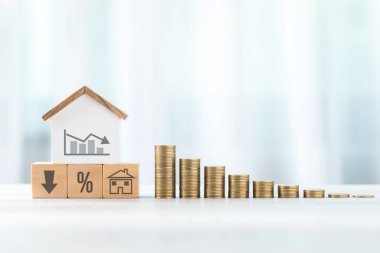 Grafiği ahşap blokların üzerinde azalan ev modeli, her biri çeşitli semboller ve madeni paralar ile işaretlenmiş. Düzenleme tasarruf, yatırım ve mali strateji kavramlarını temsil etmektedir