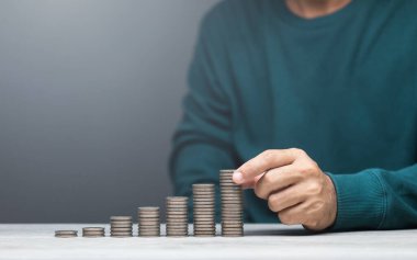 Adam bir masaya bozuk para yığıyor, en küçükten en büyüğe sıralıyor. Görüntü finansal büyüme, tasarruf ve dikkatli para yönetimini temsil ediyor