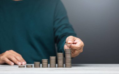 Adam bir masaya bozuk para yığıyor, en küçükten en büyüğe sıralıyor. Görüntü finansal büyüme, tasarruf ve dikkatli para yönetimini temsil ediyor
