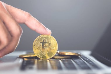 Adam bilgisayarını kullanırken altın bir Bitcoin tutuyor, çevrimiçi işlemler için Bitcoin 'i temsil ediyor, modern finansal teknoloji ve kripto kullanımı kavramını vurguluyor.