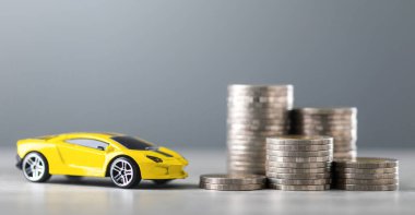 Arabaların vergi konsepti, araç sahibi olmanın getirdiği mali yükü yansıtıyor. Masadaki bir yığın para ve küçük bir araba modeli planlama ve vergiler için biriktirmeyi sembolize ediyor