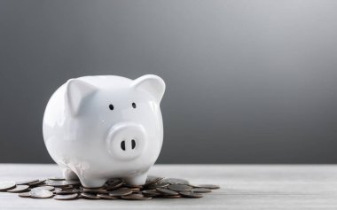 White piggy bank and a pile of coins on a wooden table against a grey background, with ample copy space for text. The image symbolizes savings, financial planning, and responsible money management. clipart