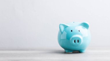 Mavi domuzcuk kumbarası, gri bir arka planda, ahşap bir masanın üzerinde duruyor, metin için geniş bir kopya alanı var. Görüntü birikimleri, finansal planlamayı ve sorumlu para yönetimini sembolize ediyor.