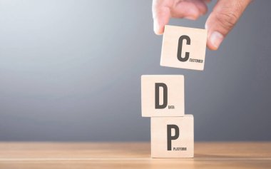 Masada C, D ve P harfleriyle ahşap blokları elle düzenlemek. Bu elementlerin entegre edilmesinin önemini vurgulayan bir müşteri veri platformu oluşturma kavramını temsil eder