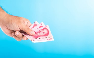 Elinde 100 Yuan 'lık banknotla, açık mavi bir masaya karşı Çin Yuan parasıyla beyaz bir kumbaranın içine bırakıyorsun. Çin 'in mali bağlamında para biriktirmek ve yönetmek