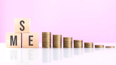 KOBİ 'nin tahtadan bir blokta yazılı olduğu ve masanın üzerinde bozuk paralar olduğu yazıyor. Küçük ve orta büyüklükteki işletmelerin mali büyümesi, yatırımın ve etkin para yönetiminin önemini vurguluyor