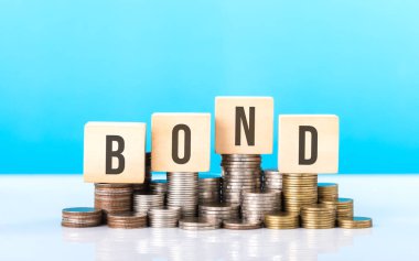 BOND etiketli ahşap bir bloğun yanında çeşitli madeni paralar yığını. Tahvil yatırımlarına bağlı istikrarlı ve yapısal büyüme, istikrar ve uzun vadeli mali planlamanın önemini vurgulamak