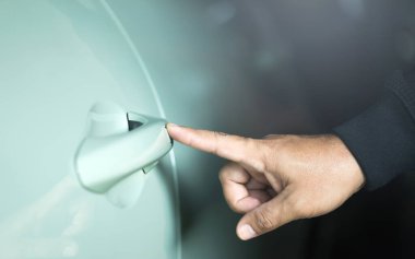 Uzaktan kumanda ya da anahtar kullanmadan açmak için bir adamın eli arabanın kapısına dokunuyor. Konfor ve güvenlik için anahtarsız giriş sistemlerinin vurgulanması, modern araç teknolojisi kavramını temsil etmektedir
