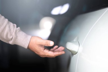 Adamın eli arabanın kapısını açmak için uzanıyor. Görüntü araç kullanımı kavramını temsil ediyor, arabaya ulaşmanın ve sorumlu bir şekilde kullanmanın günlük eylemini vurguluyor