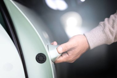 Adamın eli arabanın kapısını açmak için uzanıyor. Görüntü araç kullanımı kavramını temsil ediyor, arabaya ulaşmanın ve sorumlu bir şekilde kullanmanın günlük eylemini vurguluyor