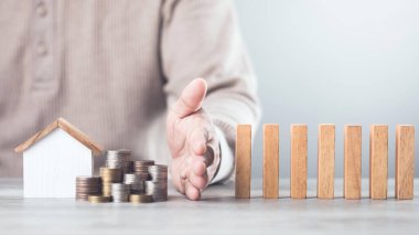 İşadamı, kaynakların etkin bir şekilde yönetilmesi, domino etkisi ve risk yönetimi alanlarında varlık ve stratejik karar alıcıların korunmasını sembolize ederek, tahta blokların düşmesini engellemek için elini kullanıyor.