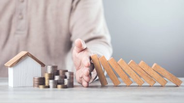 İşadamı, kaynakların etkin bir şekilde yönetilmesi, domino etkisi ve risk yönetimi alanlarında varlık ve stratejik karar alıcıların korunmasını sembolize ederek, tahta blokların düşmesini engellemek için elini kullanıyor.