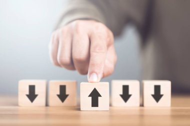 Man selecting an arrow symbol on wooden blocks, symbolizing the concept of thinking in different directions and exploring alternative perspectives in decision-making clipart