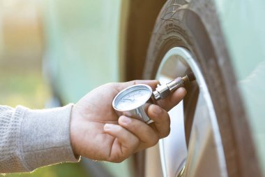 Bir araba sahibi, lastik enflasyonunu kontrol etmek için basınç göstergesi kullanır. Aracın hazır olduğunu ve yolculuğa başlamadan önce uygun lastik bakımının önemini vurgular.