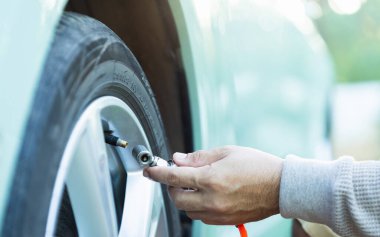 Bir araba sahibi lastik bakımı ve basınç kontrollerinin önemini vurgulayarak yolculuktan önce güvenli, sorunsuz bir yolculuk ve hazırlık için lastiği şişirir.