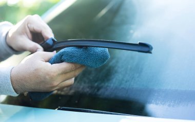 Bir araba sahibi silecekleri kumaşla temizler. Normal bakımın en iyi performans ve tüm hava koşullarında net görünürlük açısından önemini vurgular.