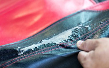 Bir araba sahibi hasarlı, sahte deri koltuk kılıfını inceler, düzenli bakım ve bakımların aracın iç kısımlarının durumunu korumak için öneminin altını çizer.