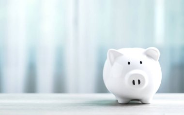 Beyaz domuz kumbarası, gri bir arka planda, ahşap bir masanın üzerinde duruyor, metin için geniş bir kopya alanı var. Görüntü birikimleri, finansal planlamayı ve sorumlu para yönetimini sembolize ediyor.