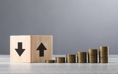 Yukarı ve aşağı okları olan tahta bloklar, düzgün istiflenmiş bozuk paraların yanında, finansal eğilimleri ve büyümeyi sembolize eden, en küçükten en büyüğe sıralanmış.