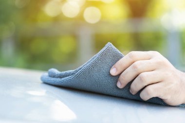 Bir araba sahibi gri bir kumaş tutuyor, aracı temizlemeye hazır. Resim, araba bakımı için doğru malzemeyi seçmenin, etkili ve nazik temizlik tekniklerinin altını çizmenin önemini vurgular